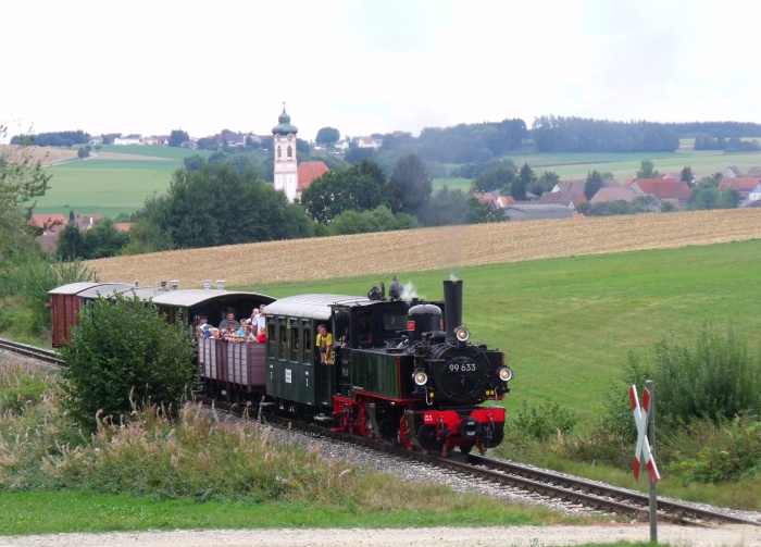 99 633 mit Zug Ochsenhausen-Warthausen, am Feldweg-Bahnübergang am Waldrand oberhalb von Reinstetten mit Kirche Reinstetten im Hintergrund, um 13:43h am 13.09.2015